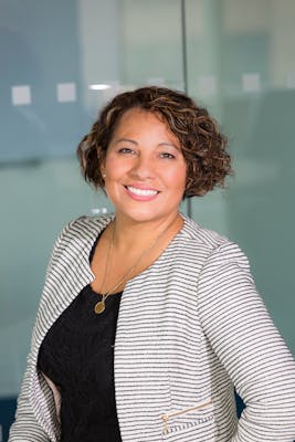 A confident woman with curly hair smiling in an office environment, conveying professionalism and approachability.