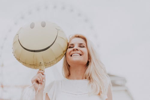 Cheerful woman holding a smiley balloon outdoors on a sunny day, exuding happiness and positivity.