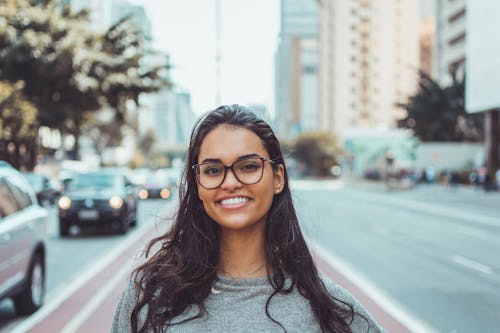 A young woman with glasses smiling on a city street, embracing urban lifestyle.