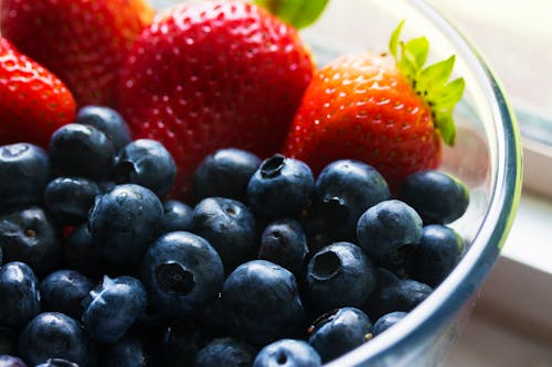 Close-up of fresh blueberries and strawberries in a glass bowl, showcasing vibrant colors and healthy appeal.