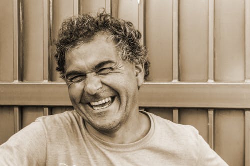 Close-up sepia portrait of a happy, laughing man against a textured background.