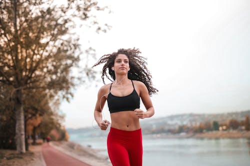 Determined woman in red leggings jogging along a scenic riverside path, embracing fitness outdoors.
