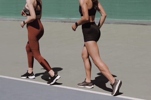 Two women walking on an outdoor track in sportswear, emphasizing healthy lifestyle and fitness.