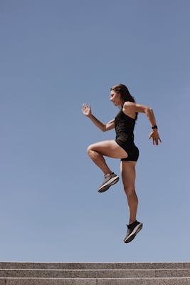 A woman in athletic wear energetically leaps up stairs against a clear blue sky.