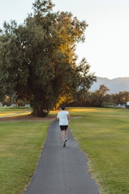 A person jogging on a serene morning path in a sunlit park surrounded by nature.