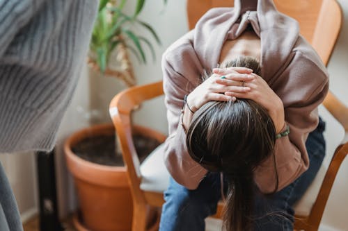 A woman sitting with her head in her hands, expressing distress inside a room.