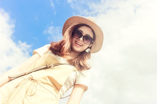 Smiling young woman in straw hat and sunglasses against a clear blue sky. Perfect summer style portrait.