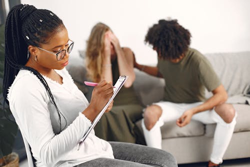 Professional advisor taking notes during a counseling session with a diverse couple in a modern setting.