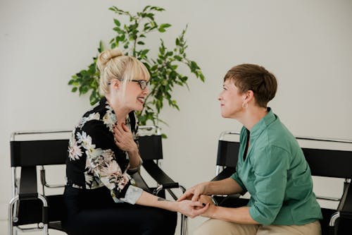 Two women sitting together, sharing a supportive and positive interaction indoors.
